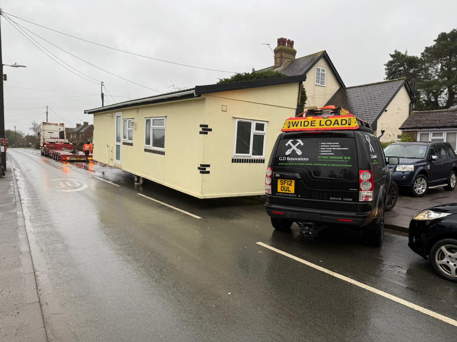 Park home moved as a wide load with an escort vehicle through a village