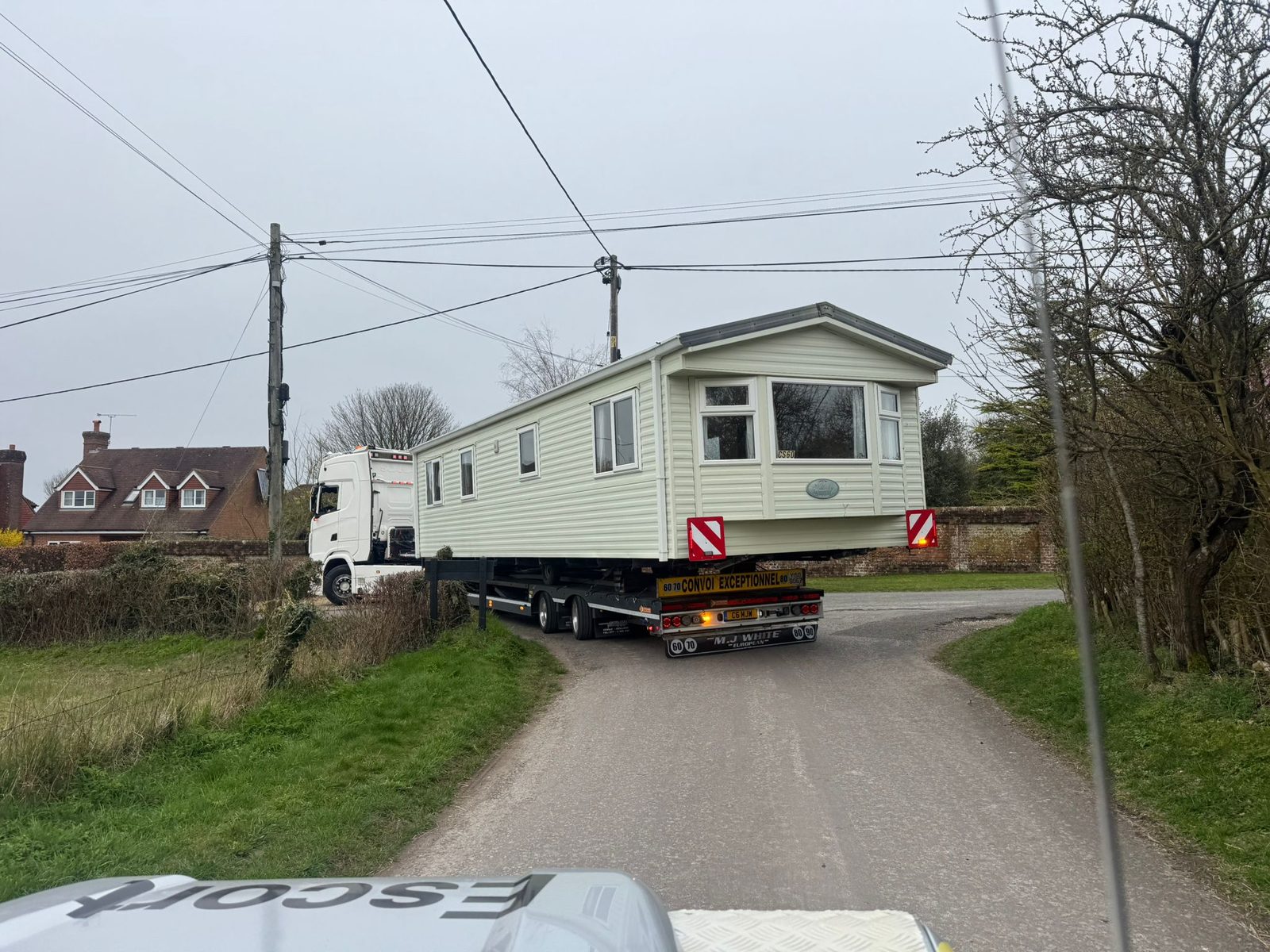 Static caravan transported on a trailer along a country lane with an escort